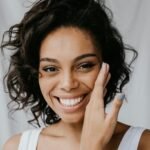A cheerful woman with curly hair and a radiant smile in a close-up portrait indoors.